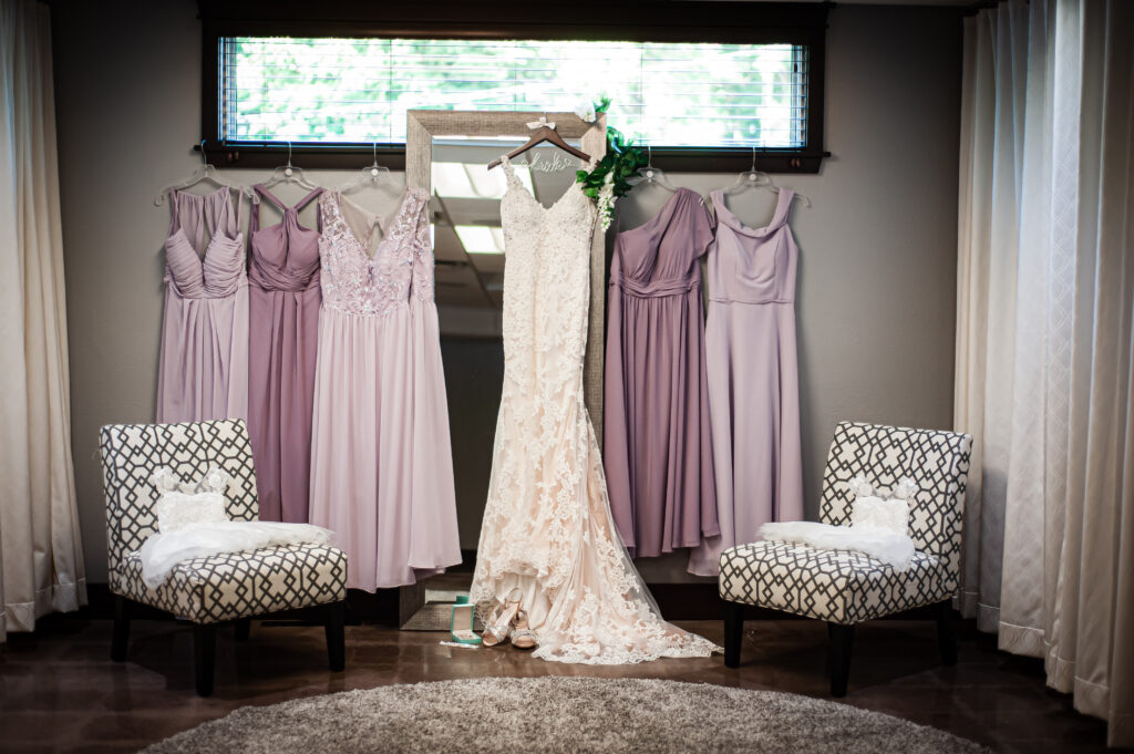 Bridal gown hangning in front of mirror with bridesmaid dresses on both sides.