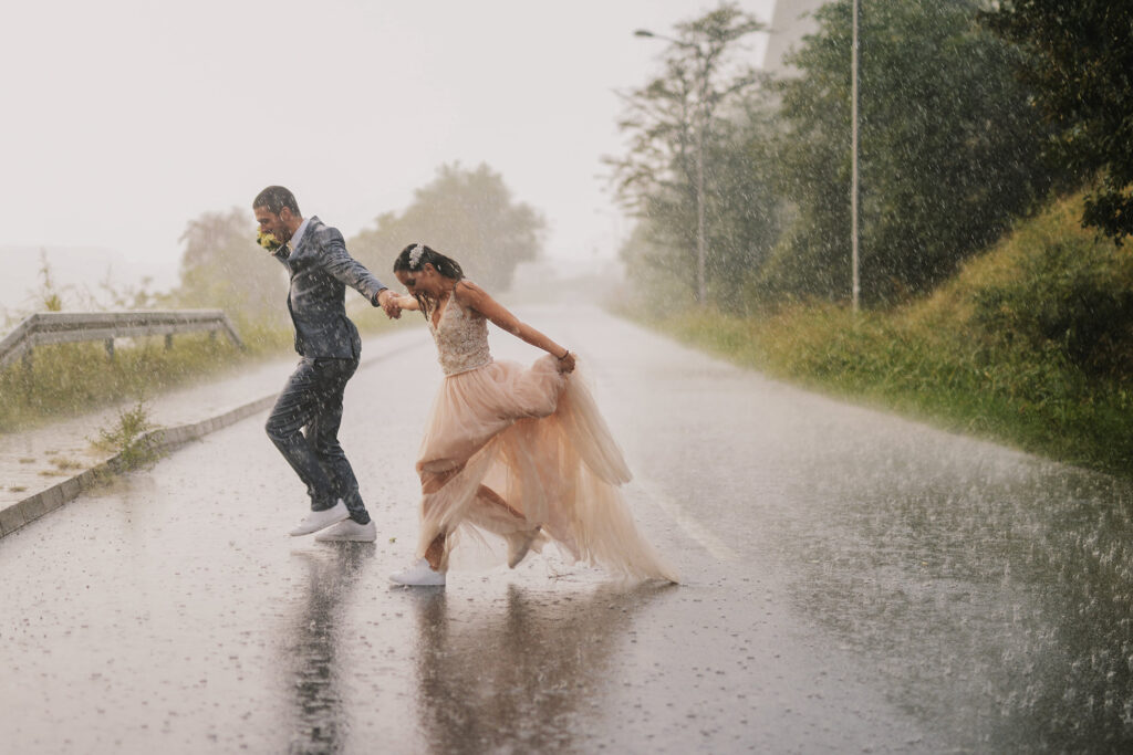 Bride and groom running across a road in the pouring rain.