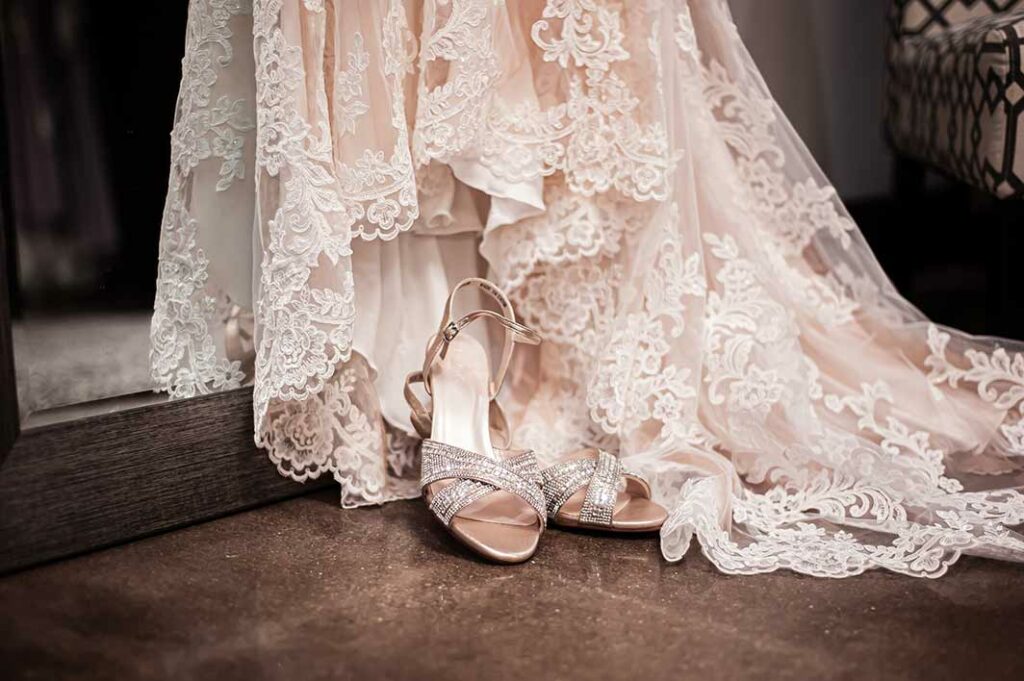 Close up of the bottom of a bridal gown with shoes laying on it.
