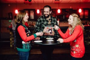 Three coworkers at an ugly sweater Christmas party making a toast.